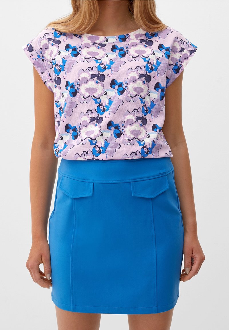 Top floreale a maniche corte nei toni del viola e del blu abbinato a una gonna blu aderente con due tasche anteriori e una texture liscia.
