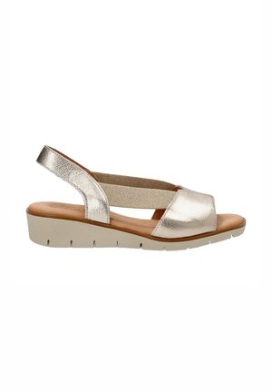 Sandalia slingback de color plata metálico con una amplia correa frontal, banda lateral elástica y suela de cuña en gris claro. Presenta una plantilla suave y texturizada.