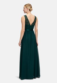 Long emerald green evening dress featuring a lace top with a deep V-back, flowing skirt, and satin waistband for added detail.