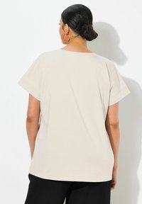 Beige krátký rukáv košile s uvolněným střihem, vybavená výstřihem do písmene U a hladkým povrchem, nošená s černými kalhotami.