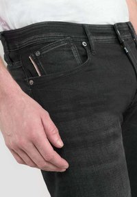 Jeans de mezclilla negra con un corte ajustado, que cuentan con un pequeño bolsillo delantero, costuras en contraste y un diseño minimalista. Textura suave.