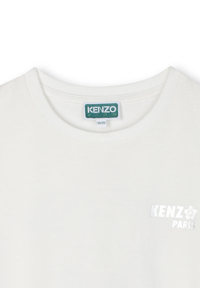 T-shirt bianca in cotone con collo rotondo, dotata di un piccolo logo in rilievo argentato "KENZO PARIS" sul lato sinistro del petto e un'etichetta verde all'interno.