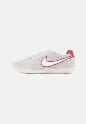 Grijze suède sneaker met witte en kastanjebruine accenten, voorzien van een opvallende witte Nike swoosh en een gestructureerde rubberen zool.