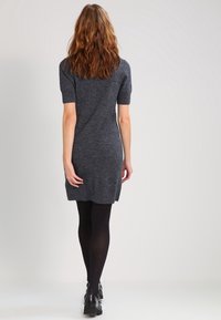 Abito a maglia grigio scuro a maniche corte con vestibilità rilassata, lunghezza fino al ginocchio, caratterizzato da un collo rotondo e una sottile texture. Indossato con collant neri e stivaletti.