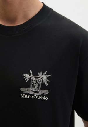 Czarna koszula z białym haftowanym kieliszkiem koktajlowym, słomką i liśćmi palmy nad napisem "Marc O'Polo" na klatce piersiowej.