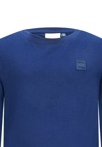 Niebieska, długorękawowa koszula z miękkiego materiału, z okrągłym dekoltem i małą prostokątną naszywką marki na klatce piersiowej.