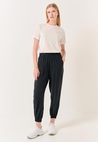 Lichtbeige t-shirt met korte mouwen en zwarte joggers met elastische taille, met taps toelopende boorden, gecombineerd met witte sneakers op een neutrale achtergrond.