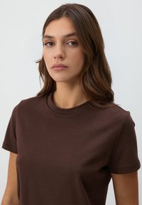 T-shirt in cotone marrone con scollo rotondo classico e maniche corte, con una texture liscia e uniforme e senza motivi o accenti visibili.