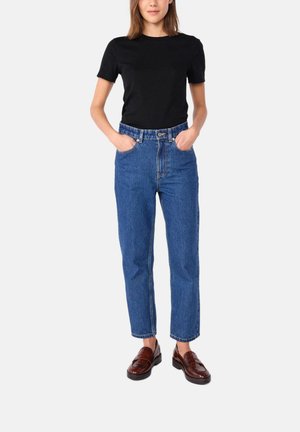 Zwarte t-shirt met korte mouwen, gecombineerd met high-waisted blauwe jeans. De jeans hebben een klassieke snit en subtiele vervaging, aangevuld met bruine loafers.