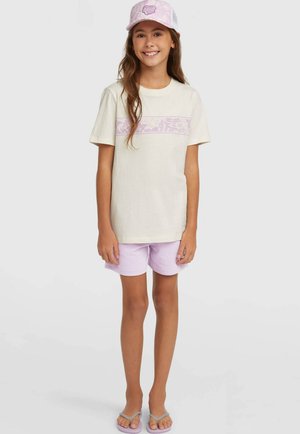 Beige bomulds-t-shirt med et lyse lilla tropisk mønster over brystet, kombineret med lilla shorts og grå klipklapper samt en matchende kasket.