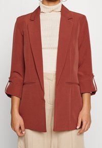 Rostfärgad kavaj med skräddarsydd design, enkel knappstängning och uppvikta ärmar. Tillverkad i ett mjukt tyg med två framfickor.