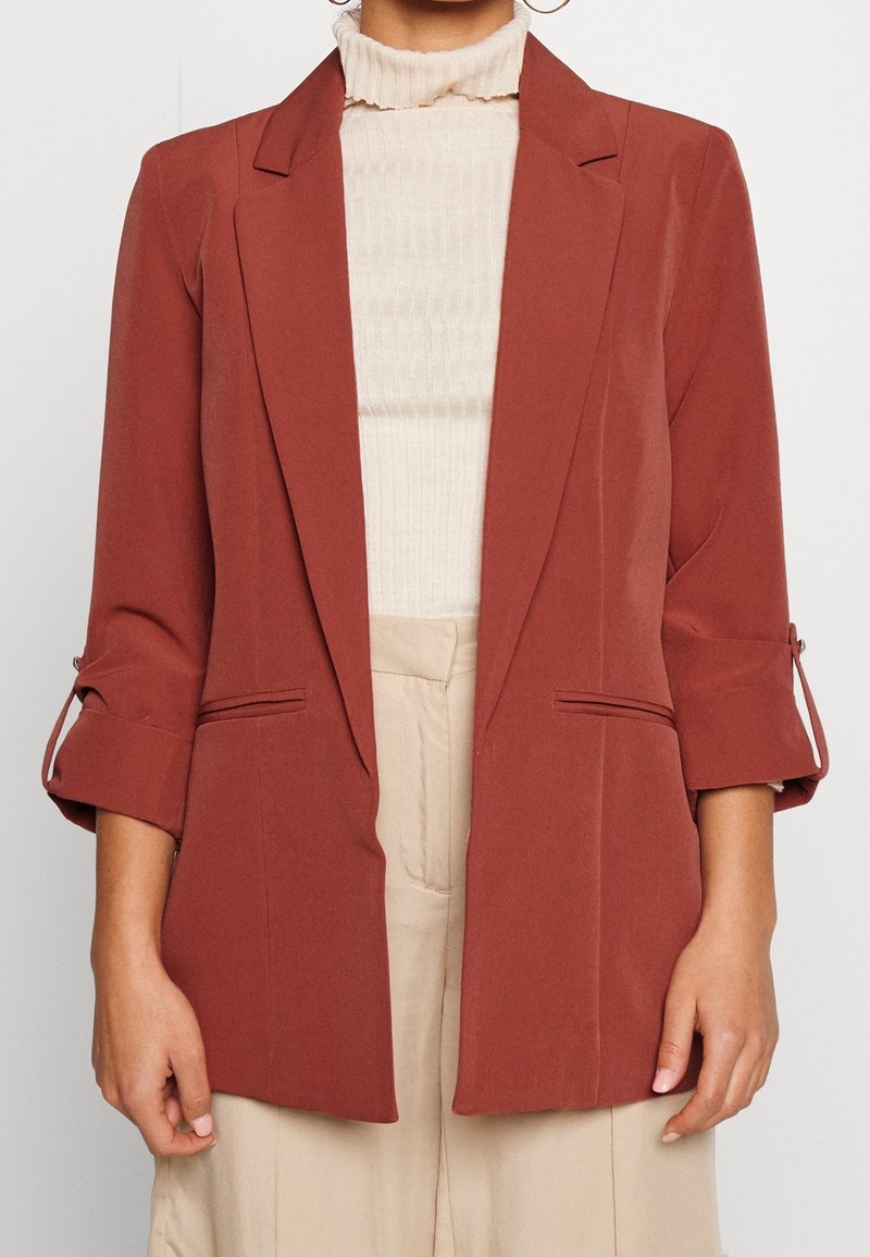 Rostfärgad kavaj med skräddarsydd design, enkel knappstängning och uppvikta ärmar. Tillverkad i ett mjukt tyg med två framfickor.