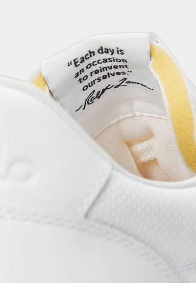 Interior view of a white sneaker showing a fabric label with the quote: "Each day is an occasion to reinvent ourselves."