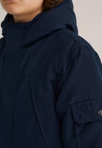 Sötétkék párnázott dzseki kapucnival, cipzáros elülső résszel, oldalzsebekkel és kiemelkedő varrás részletekkel. Puha tapintású és tartós anyagból készült.