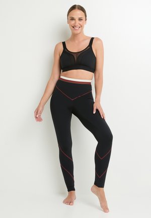 Reggiseno sportivo nero con pannelli in rete e spalline larghe, abbinato a leggings neri con cuciture rosse a contrasto e una vita bianca.