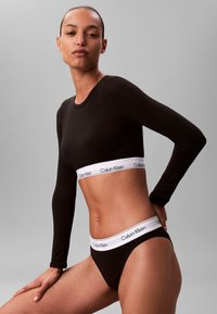 Black long-sleeve top with a white Calvin Klein logo band, paired with matching black briefs featuring the same logo on the waistband.