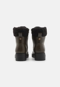 Bottines en cuir marron avec col en peluche noir, talon et semelle en caoutchouc texturé. Comprend une languette arrière et des accents métalliques décoratifs.