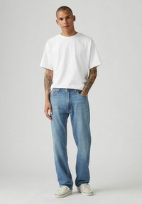 Camiseta blanca de manga corta combinada con jeans de mezclilla azul claro. La camiseta es sencilla y tiene un corte relajado, los jeans presentan un diseño clásico de cinco bolsillos.