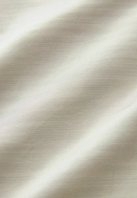 Tessuto beige chiaro con una trama liscia e un motivo a strisce sottile, che mostra un drappeggio morbido e una finitura leggermente lucida.