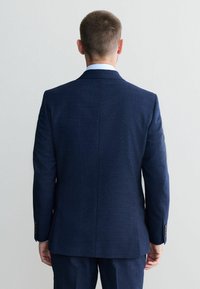 Marineblauw op maat gemaakte pak met een gestructureerde afwerking, voorzien van een enkele split aan de achterkant, knoopsluiting bij de mouwen en een slanke silhoeët.