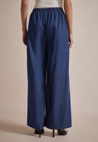 Pantalones de mezclilla de pierna ancha en un tono azul oscuro. Presentan una cintura elástica y una textura suave, con piernas de longitud completa y sin adornos.