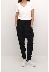 Pantalons de jogging noirs amples avec poches latérales, chevilles resserrées et taille élastique, associés à un t-shirt blanc à col en V et des baskets blanches.