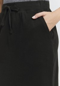 Jupe noire côtelée avec une taille élastique et un cordon de serrage. Elle a des poches latérales et une texture douce.