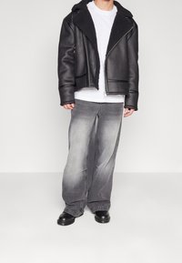 Sort læderjakke med krave i shearling, kombineret med grå, falmede jeans med vide ben og sorte chunky støvler. Enkel hvid t-shirt under.