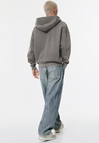 Gray hoodie with a relaxed fit, featuring a hood and ribbed cuffs, paired with light blue striped wide-leg jeans. White sneakers.