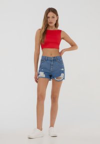 Cropped top rosso con scollo quadrato, abbinato a pantaloni shorts di jeans strappati. Sneakers bianche completano il look casual.