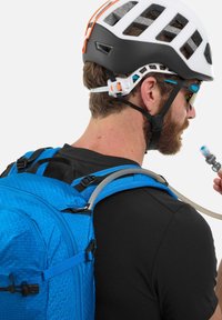 Blauer Rucksack mit sechseckigem Muster und einem Trinkschlauch, über einem schwarzen Shirt getragen. Ein weißer und schwarzer Helm ist ebenfalls sichtbar.