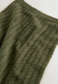 Grüner Strickstoff mit einem strukturierten, gerippten Design. Weiches, gemütliches Material in einem warmen, gedämpften Farbton.
