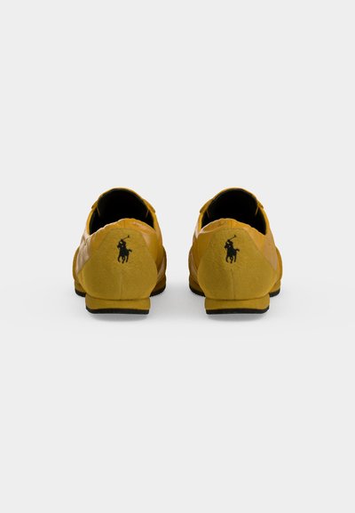 Paire de chaussures décontractées jaunes vues de dos avec un logo noir de cheval et cavalier sur chaque talon.
