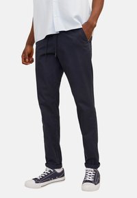 Pantalon en coton marine avec une coupe décontractée, doté d'une taille élastique avec un cordon de serrage, de poches latérales et de manches repliées, associé à des baskets blanches.