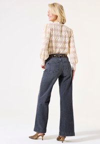Helle beige Bluse mit Blumenmuster und Puffärmeln, kombiniert mit weiten dunkelblauen Jeans und einem Gürtel im Leopardenmuster. Getragen mit metallischen Absatzschuhen.