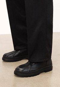 Czarne skórzane buty z fakturowaną powierzchnią, z zaokrąglonym noskiem, przeszyciami na cholewce oraz solidną gumową podeszwą.