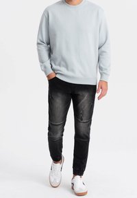 Ljusblå crewneck sweatshirt, svarta slitna jeans, och vita sneakers med svarta accentuerningar. Avslappnad outfit med enkel design och texturer.