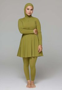 Olijfgroene zwemjurk met lange mouwen, hoge kraag en geplooide rok, gecombineerd met bijpassende leggings. Het materiaal voelt soepel en rekbaar aan.