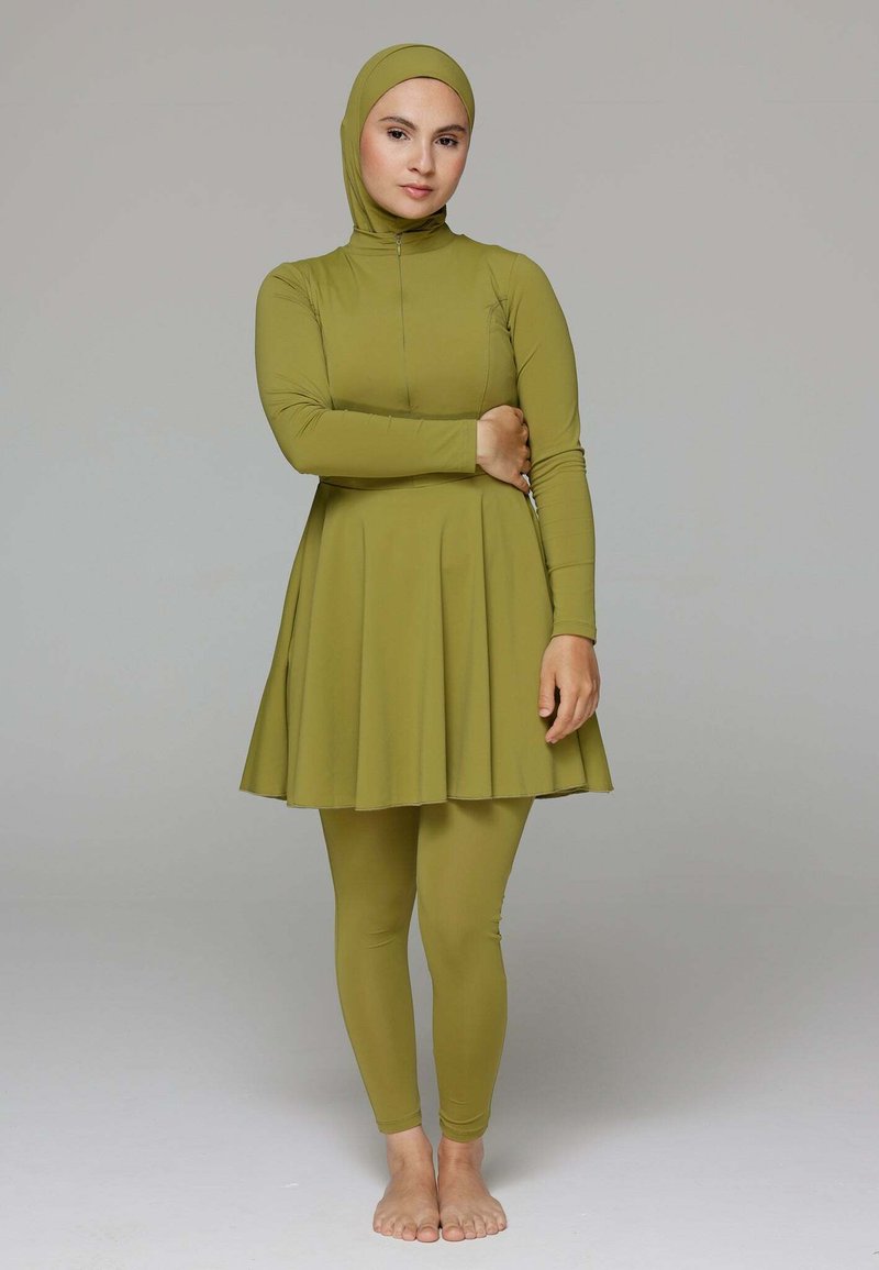 Olijfgroene zwemjurk met lange mouwen, hoge kraag en geplooide rok, gecombineerd met bijpassende leggings. Het materiaal voelt soepel en rekbaar aan.