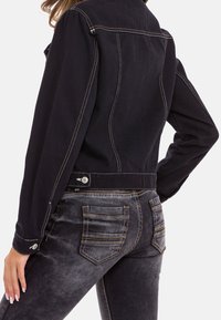 Schwarze Jeansjacke mit sichtbaren Nähdetails, kombiniert mit grauen Jeans mit Gesäßtaschen und kontrastierendem Faden.