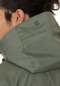 Olive green waterproof jacket with a high collar, featuring a stitched design and a small logo on the back. Texture appears smooth.