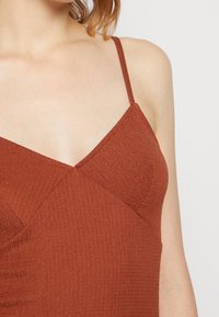 Rustinvärinen mekko, jossa on ohuet hihat, ribbipinta, V-mallinen kaula-aukko ja vinot saumat rinnassa rakenteellista yksityiskohtaisuutta varten.