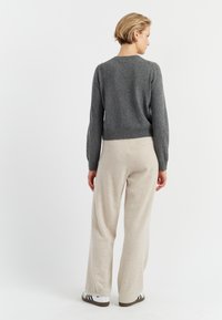 Maglione grigio in misto lana con scollatura rotonda e maniche lunghe, abbinato a pantaloni beige a gamba larga e sneakers bianche con strisce nere.