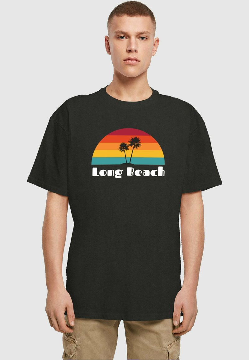 Svart T-skjorte med et fargerikt solnedgangsdesign med horisontale striper i rødt, oransje, gult og turkis, sammen med to palmer og teksten "Long Beach".