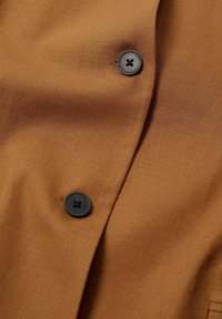 Tissu marron avec deux boutons noirs à quatre trous cousus, montrant la texture et les détails de la couture.