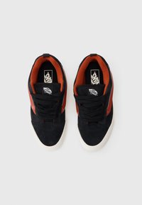 Crne suede tenisice s crvenim detaljima, s bijelom gumiranom potplatom, vezanjem i podstavljenim ovratnikom za udobnost. Vidljiv Vans logo.