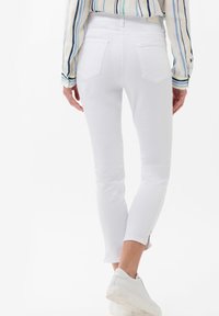 Vita skinny jeans med en figurnära design. Har bakfickor och en avskuren kant med sidoklyftor. Bärs med vita slip-on sneakers.