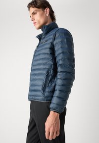 Giacca puffer blu navy con colletto alto, design a righe orizzontali, chiusura con zip frontale e branding discreto sul petto. Materiale liscio e lucido.