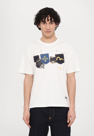 T-shirt en coton blanc présentant un design graphique de différentes formes de poches en bleu, noir et or, avec des détails de couture contrastants.