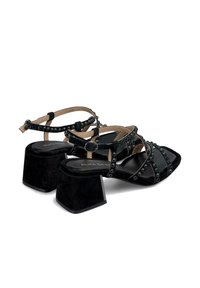 Schwarze Wildleder-Sandalen mit Blockabsatz, über Kreuz gefasst und dekorativ mit Nieten akzentuiert. Offene Zehenpartie mit verstellbaren Knöchelriemen.